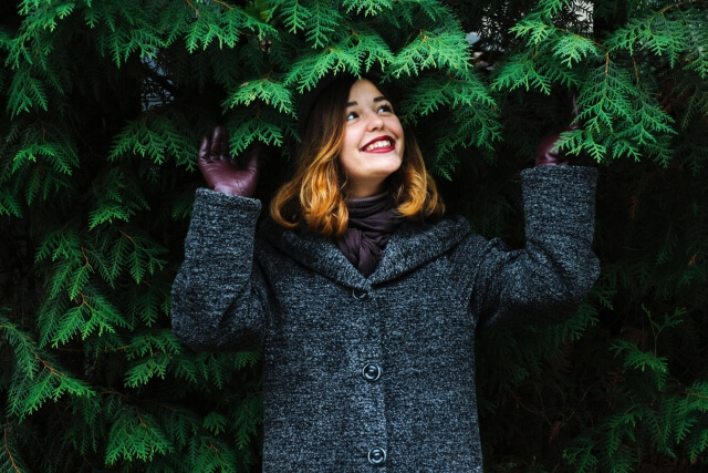 木の下にいるグレーのコートを着た笑顔の外国人女性